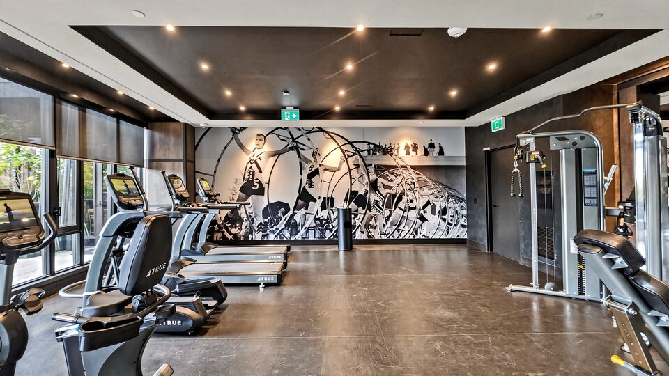 Residents' gym with treadmills, bikes and weight machines in front of a black and white mural